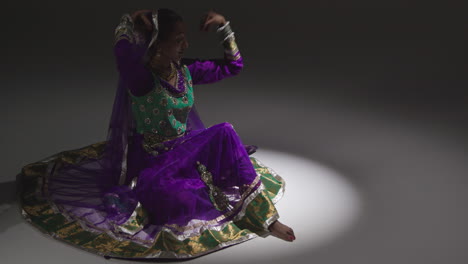 bailarina de kathak femenina realizando un baile vestida con el vestido tradicional indio sentada en el suelo en el centro de atención 3