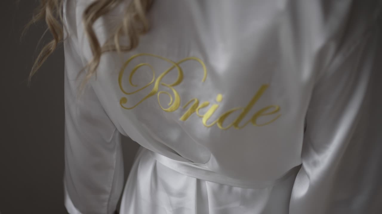 Close-up of a white satin bridal robe with "Bride" embroidered in gold, worn by the bride, highlighting her special role on the wedding day