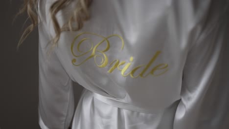 close-up of a white satin bridal robe with "bride" embroidered in gold, worn by the bride, highlighting her special role on the wedding day