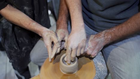 dos personas formando arcilla en una rueda de cerámica