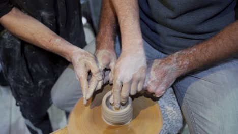 two people shaping clay on a pottery wheel