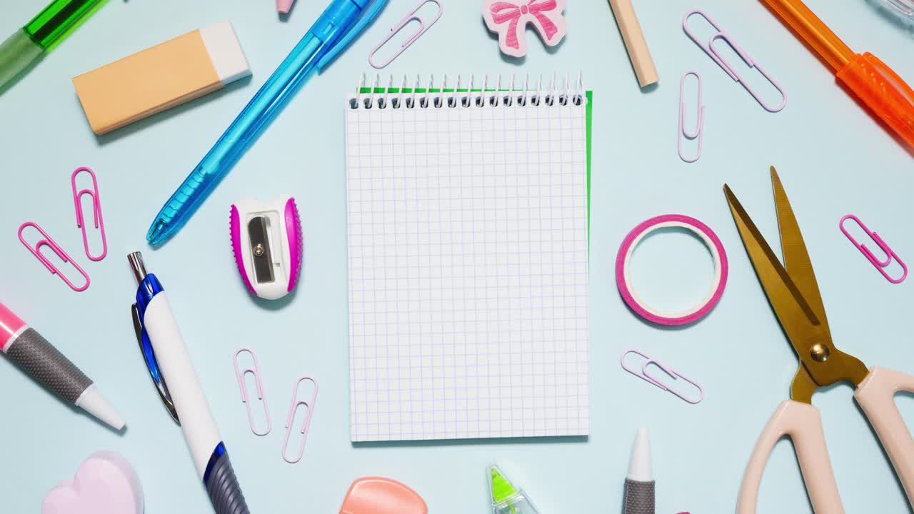 Top down stop motion of colorful supplies circling a small grid notebook on light blue, leaving center copy space in a seamless loop