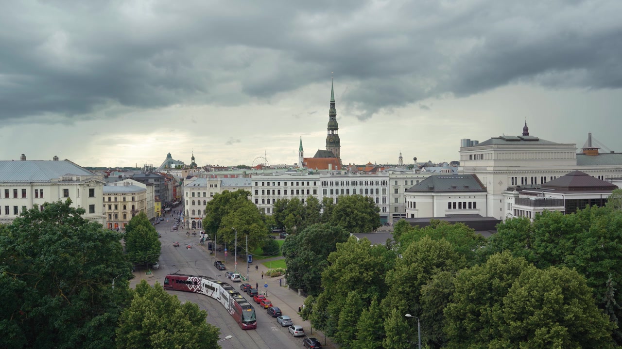 Vista panoramica dello skyline della Città Vecchia di Riga con la guglia della Chiesa di San Pietro e un tram sotto nuvole temporalesche.