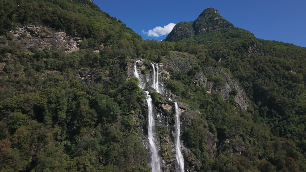 Drone che vola verso le spettacolari cascate dell'Acquafraggia che scendono da una montagna verde in Val Bregaglia, Italia. Ripresa aerea frontale.