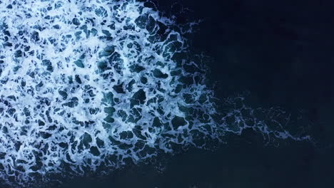 straight down aerial view of a wave breaking with bubbles and sea foam creating an abstract white water pattern in the water