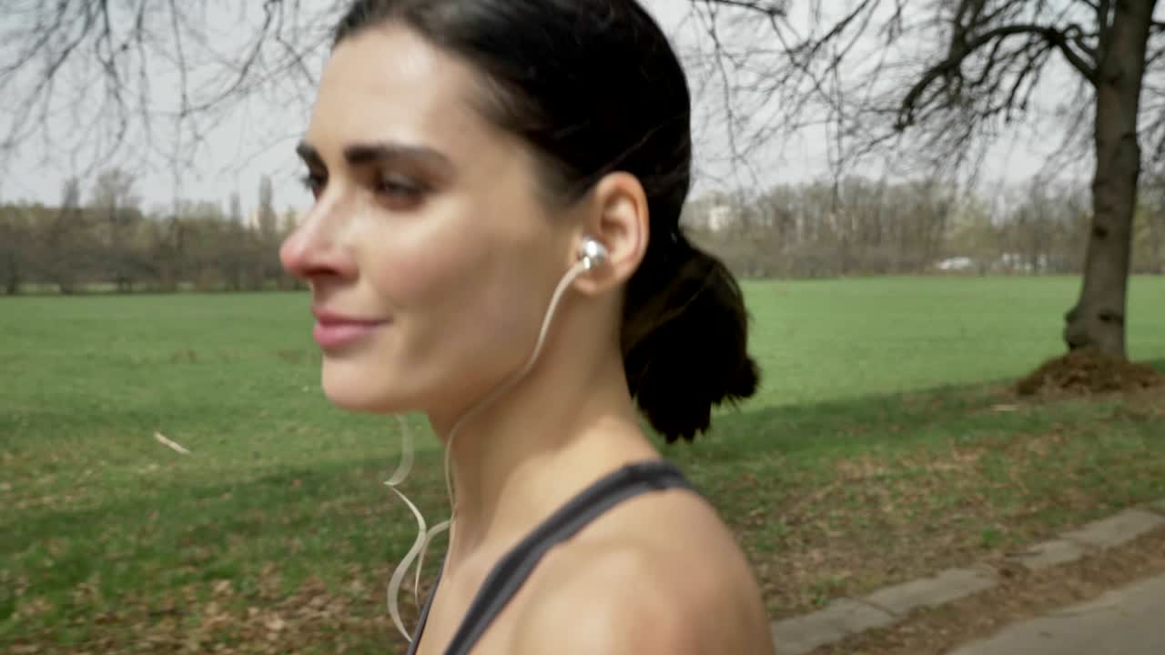 Young happy sport girl is running with earphones in park in summer, healthy lifestyle, sport conception, side view