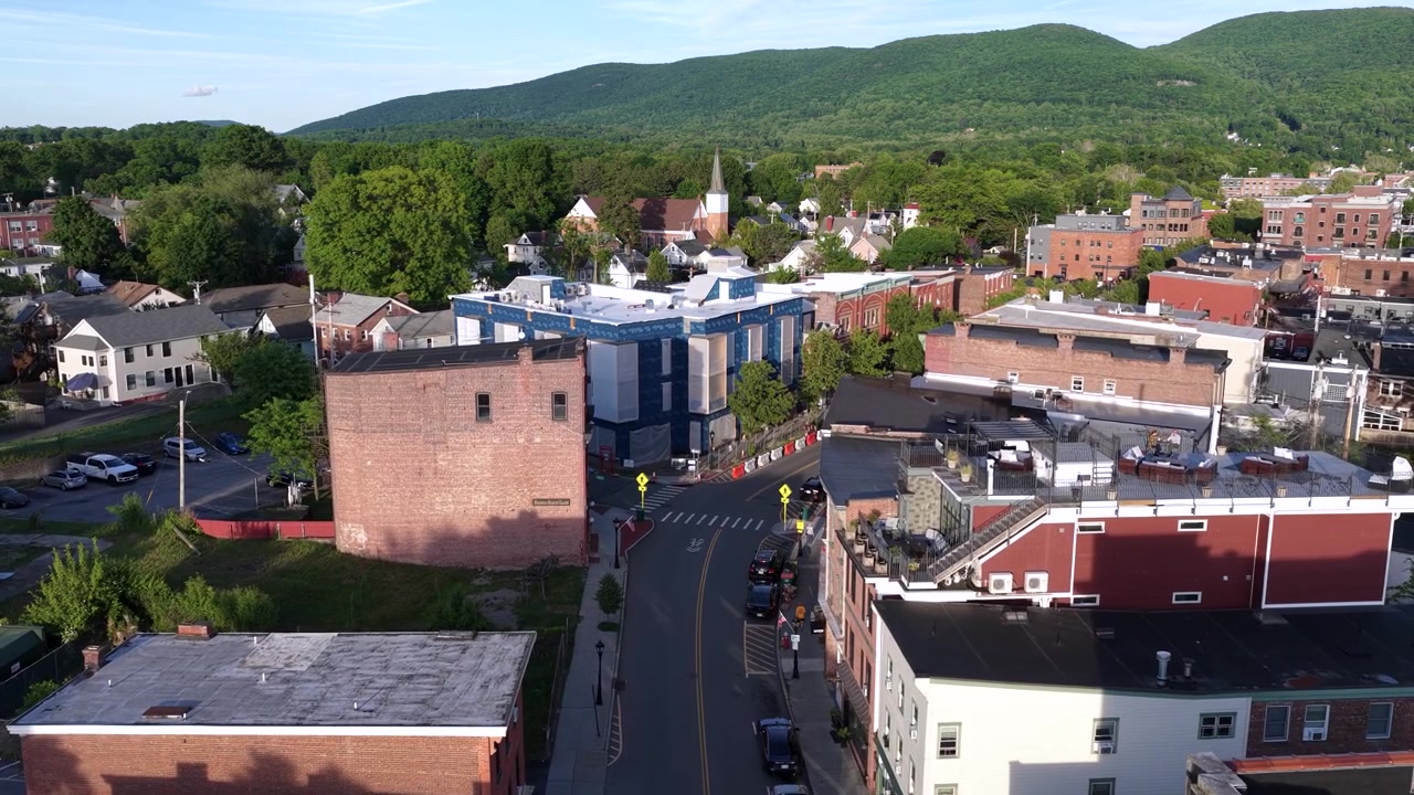 Vista aérea da Main Street em Beacon, Nova York, ao pôr do sol. Um edifício em construção e prédios de tijolos são visíveis, assim como as montanhas distantes.