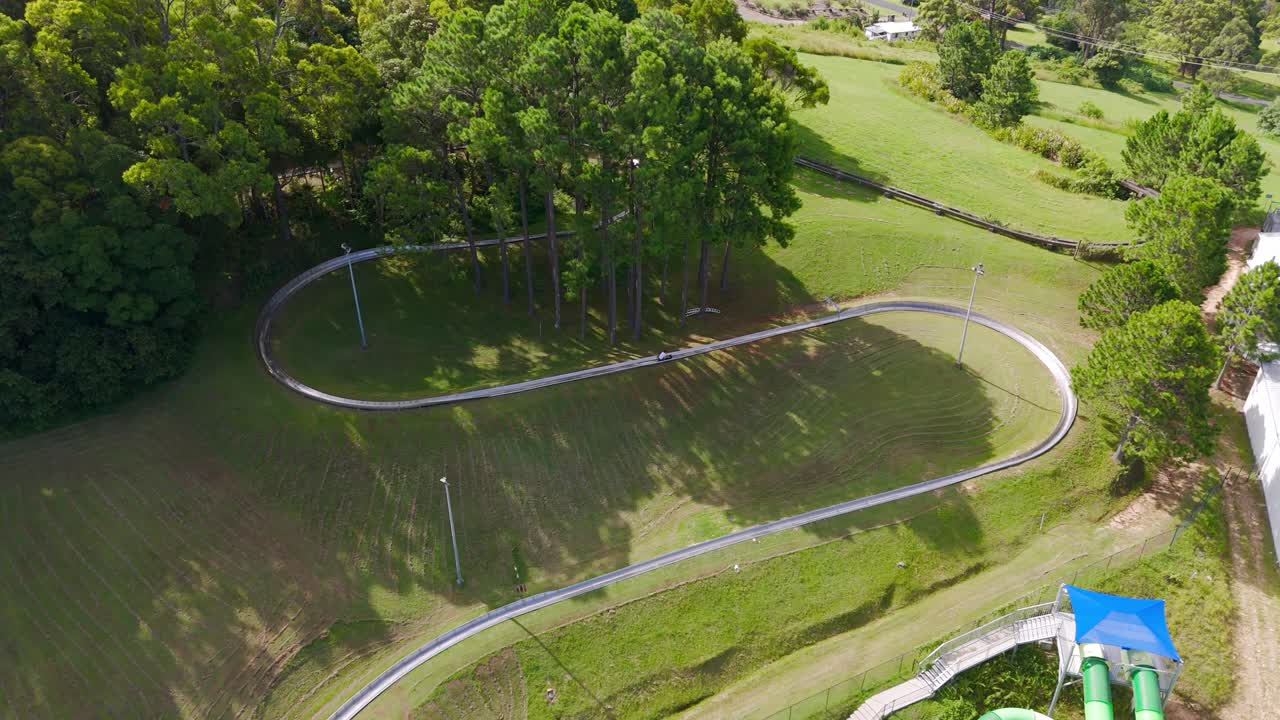 Aerial: person riding a toboggan during the day at The Big Banana Fun Park in Coffs Harbour, New South Wales, Australia, orbit drone shot