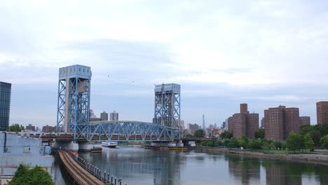 stationary ground shot of commuter train going over the park avenue bridge as a tour boat passes on the harlem river underneath, between the bronx and harlem manhattan new york city