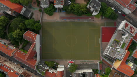 Aerial-birds-eye-overhead-top-down-view-from-ascending-drone.-Rocket-shot-of-football-playground-closely-surrounded-by-buildings.-Berlin,-Germany.