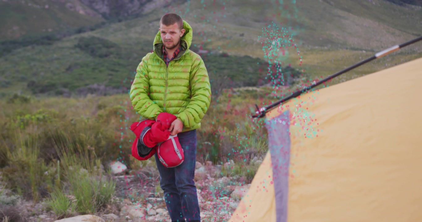 Male camper examining straps and releasing red sleeping bag for camping setup by yellow tent