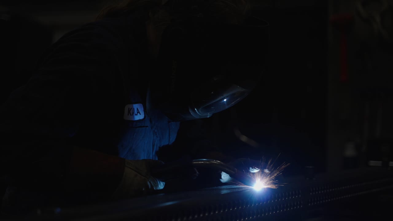 Slow mo, blue collar worker welding metal, bright sparks in dark workshop room