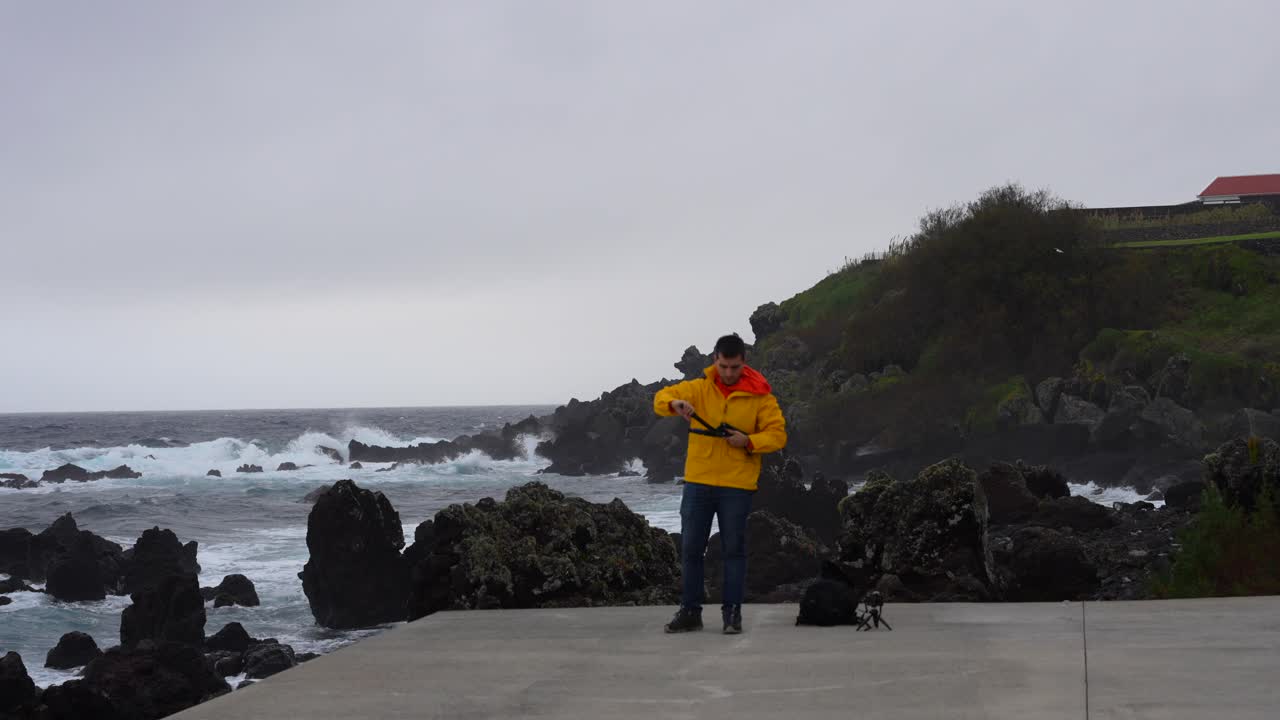 아조레스 제도의 테르다에서 대서양의 파도와 함께 바위가 있는 해안에 삼각대를 세우고 있는 남자