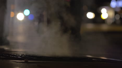 Gente-Caminando-Sobre-Un-Desagüe-Humeante-En-La-Ciudad-De-Noche