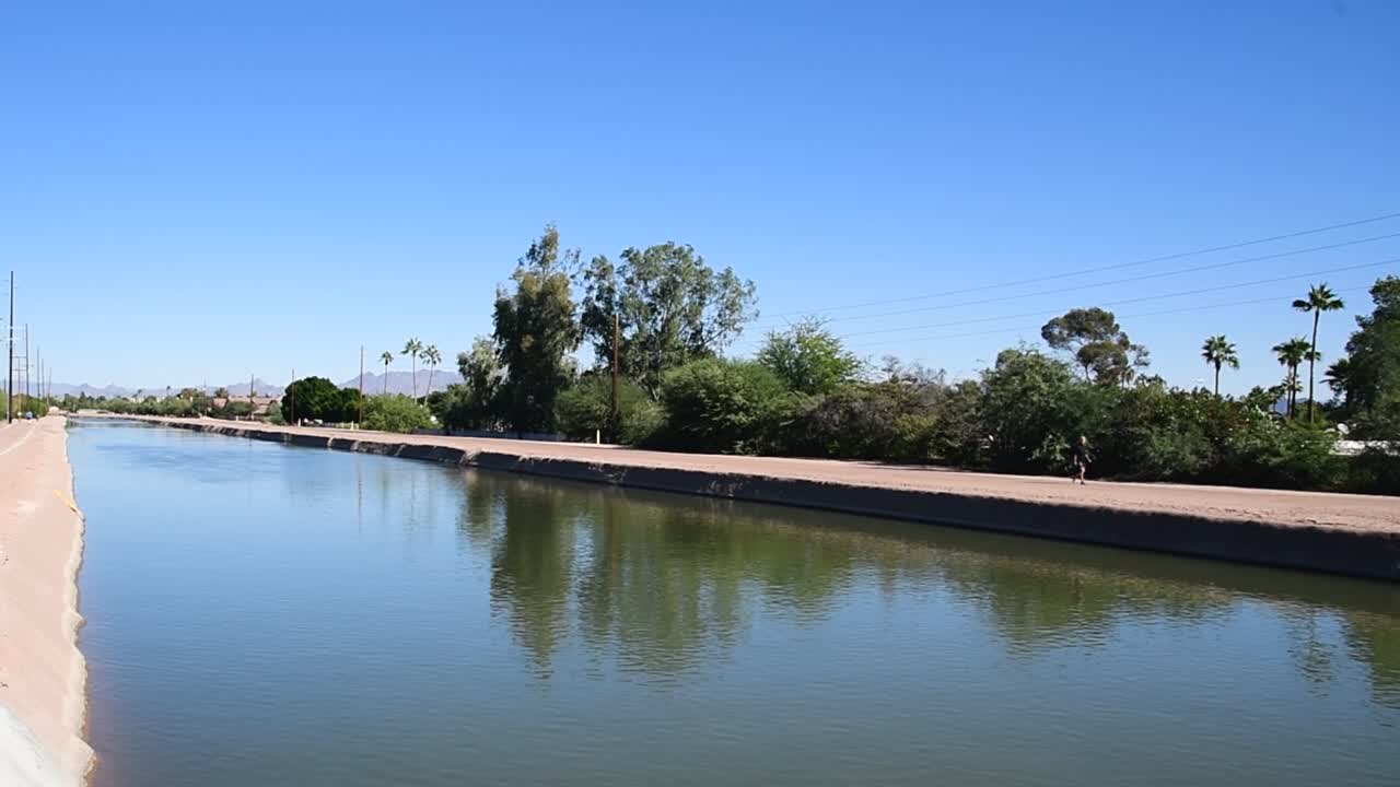 Pan from walker on the far side of the Arizona Canal Trail to the near side people walking their dog, Scottsdale, Arizona.