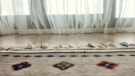 alfombra beige con patrón decorativo cerca de una ventana con cortinas transparentes.