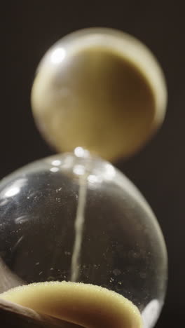 vertical clip of hourglass sand flowing in 100fps slow motion. time running out