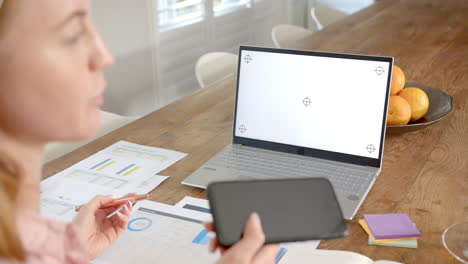 holding smartphone, woman working from home with laptop and documents on table, copy space