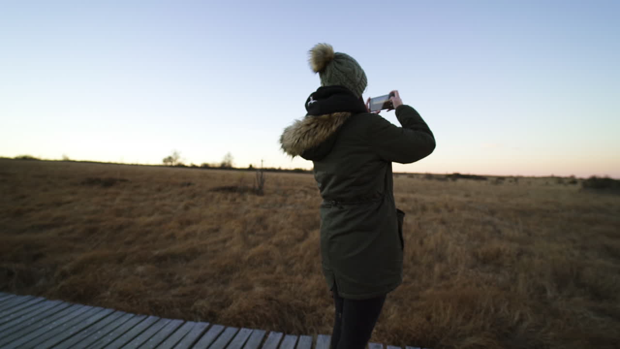Beautiful female taking video of natural marsh from wooden pathway, orbit view