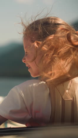 happy little girl with long hair waved by wind rides fast motorboat in tranquil sea bay. joyful child sails modern yacht in ocean on sunny day