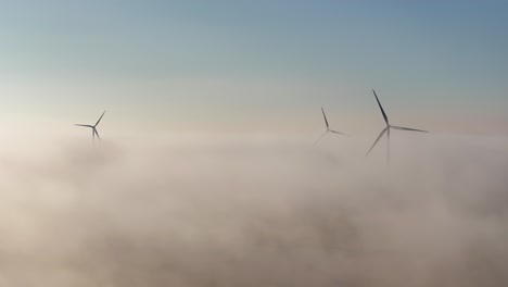 drone view of wind mills at sunrise as low lying fog blankets the surrounding farmland