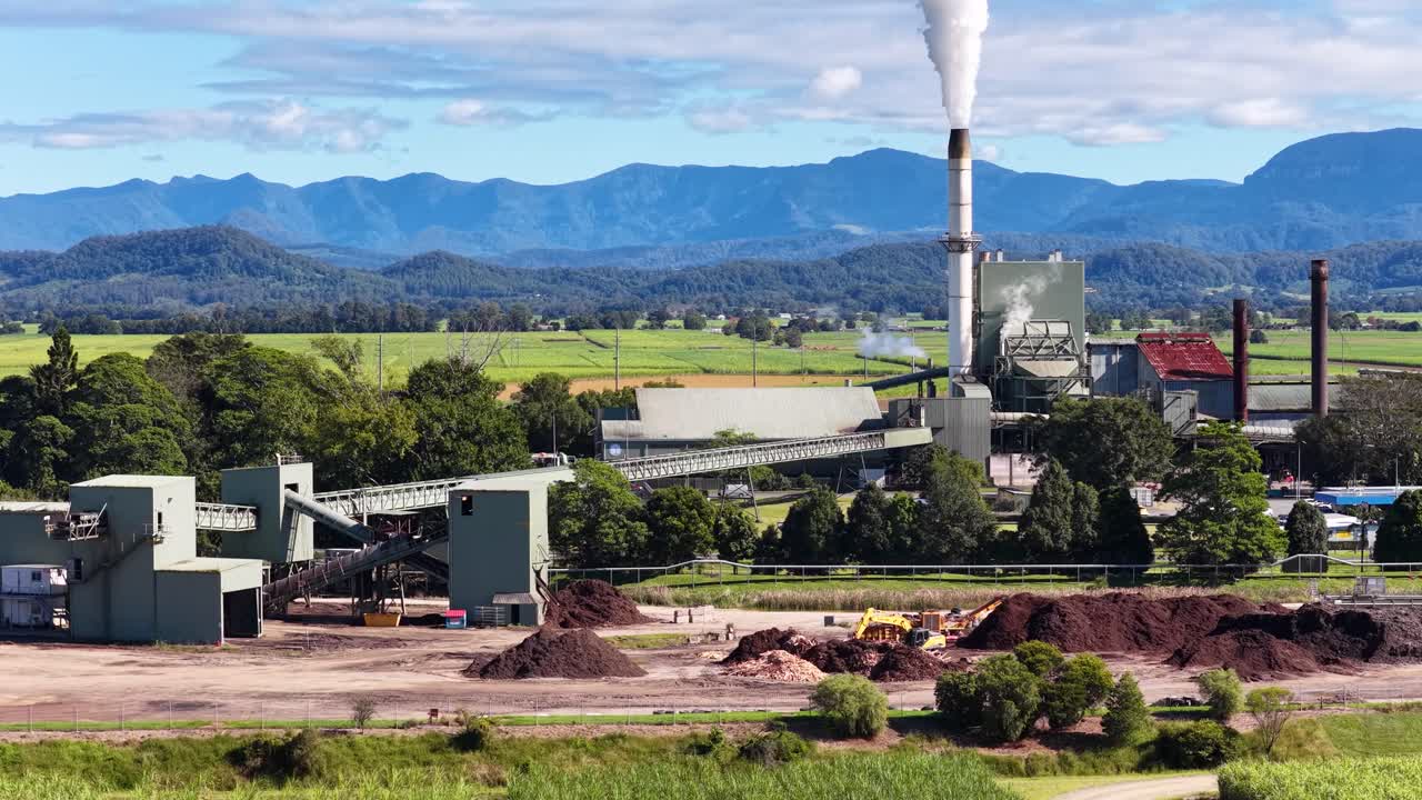 Drone footage of a factory with smoke stacks in a rural landscape, highlighting environmental impact and industrial activity