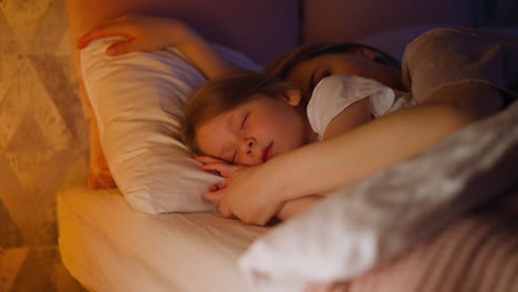 sleepy mother embraces daughter lying together in bed