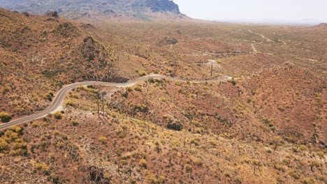 Droneshot-Volando-Hacia-Arriba-Mientras-Un-Auto-Blanco-Conduce-A-Través-De-Un-Típico-Paisaje-Desértico-Occidental-En-4k