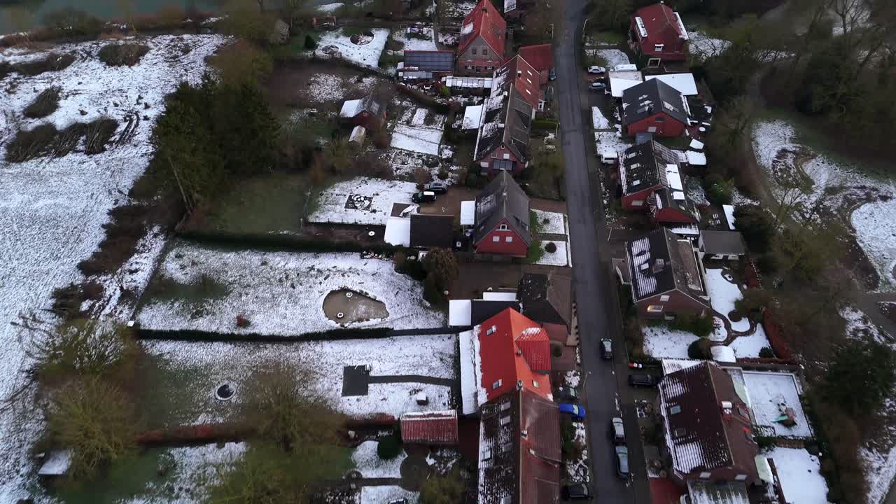 Straight street of housing area with snowy garden near lake in winter season. Aerial top down flyover shot. Cloudy day in american suburb neighborhood.