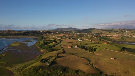 flight at the mouth of a river to the sea in a rural area with green meadows and scattered houses and in the river we see a pier with its boats with a day of blue sky in summer in cantabria spain
