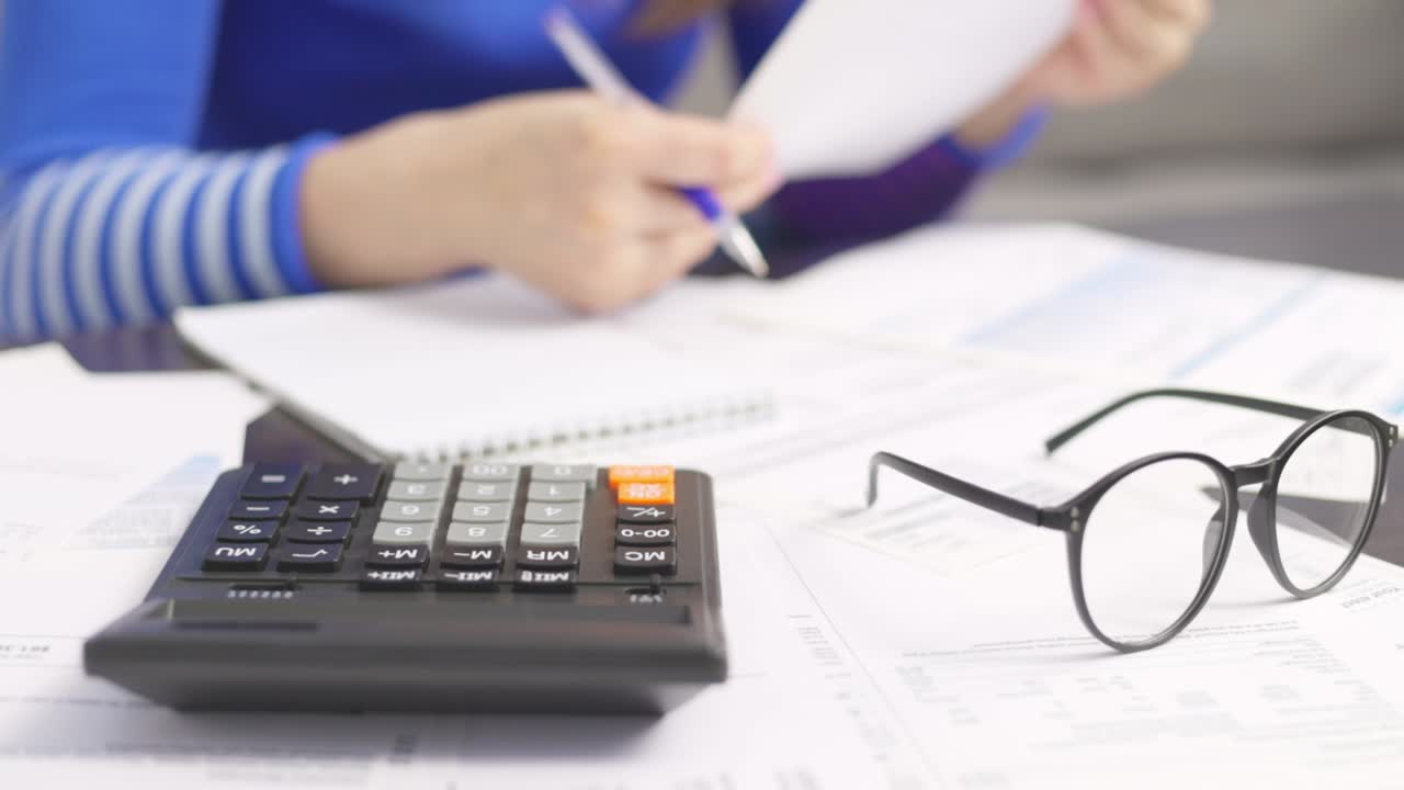 mujer usando calculadora para calcular facturas domésticas en el hogar, haciendo papeleo para pagar impuestos