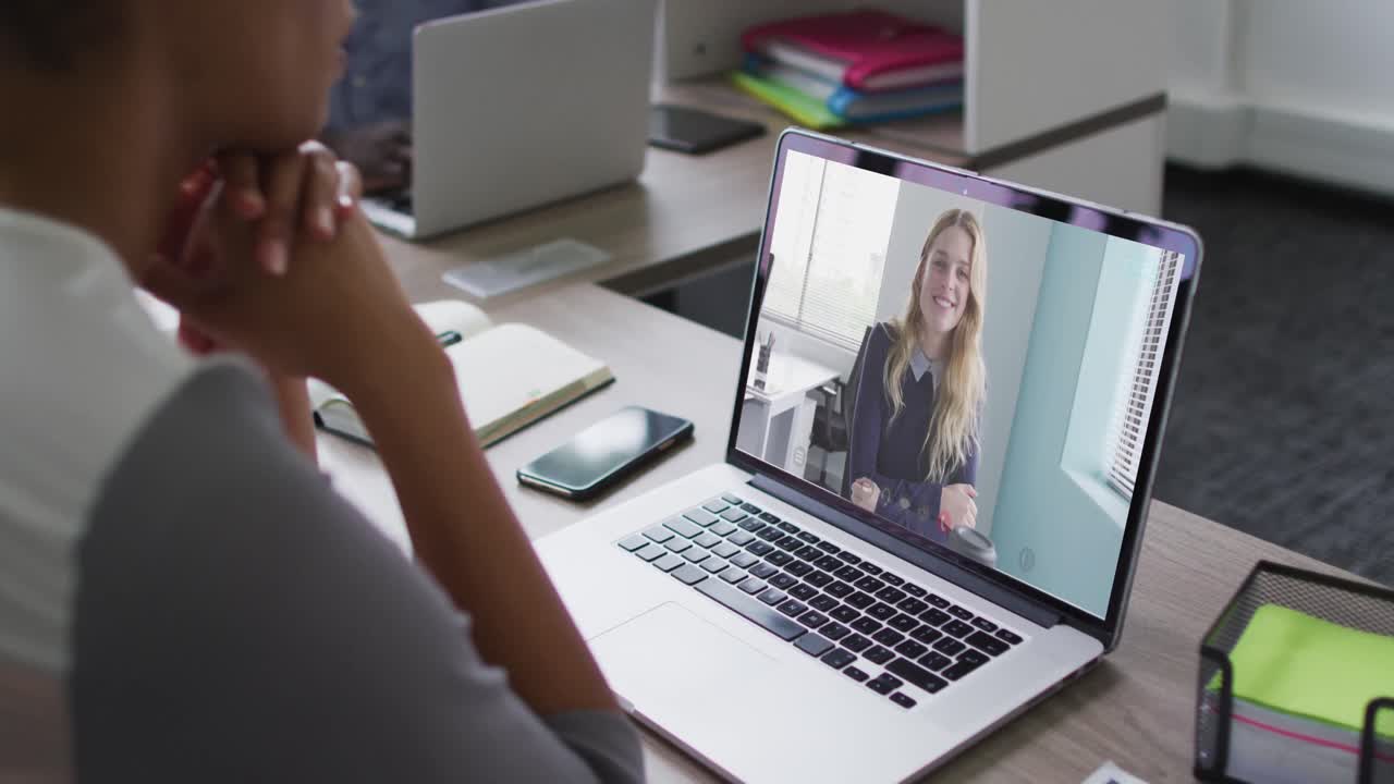 African american businesswoman sitting at desk using laptop having video call with female colleague