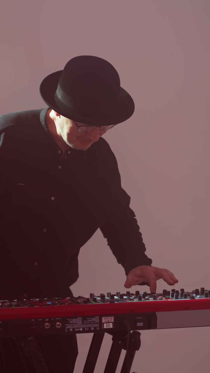 hombre con traje negro y sombrero juega sampler rojo contra un telón de fondo rosado vibrante, enfocado y artístico