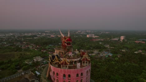 Drone-flighting-away-from-the-iconic-Wat-Sam-Phran-in-Bangkok,-Thailand,-revealing-the-beauty-of-Bangkok-in-the-horizon