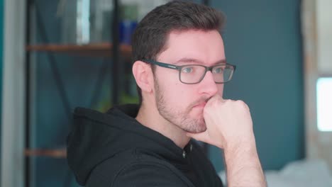 Pensive-young-man-sitting-pondering-in-living-room