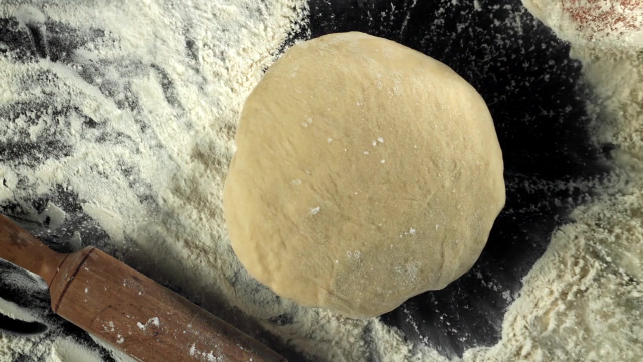 Panetto di impasto fresco con farina e mattarello su superficie nera