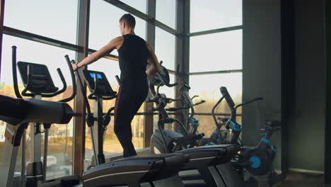 Portrait-fitness-man-warm-up-before-training-on-elliptical-cross-trainer-in-gym-club.-Close-up-male-training-cardio-exercise-on-cross-trainer-in-fitness