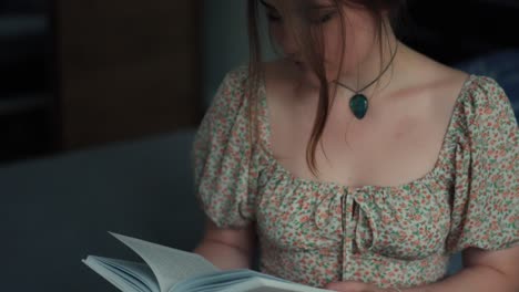 una joven hermosa en un vestido se está concentrando en leer un libro en casa
