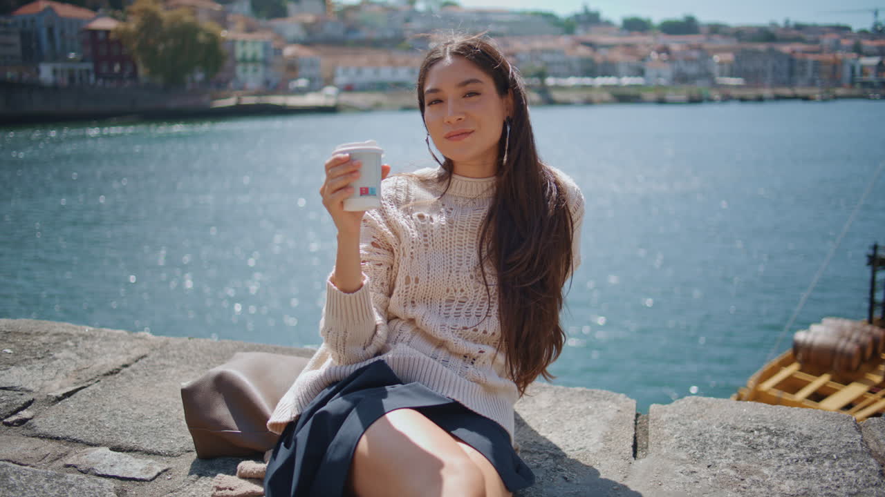 Attractive woman drinking latte takeaway in sunbeams canal. Lady looking camera