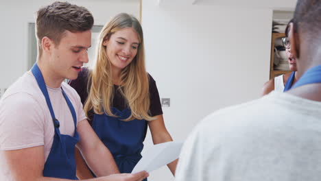 Male-And-Female-Adult-Students-Looking-At-Recipe-In-Cookery-Class-In-Kitchen