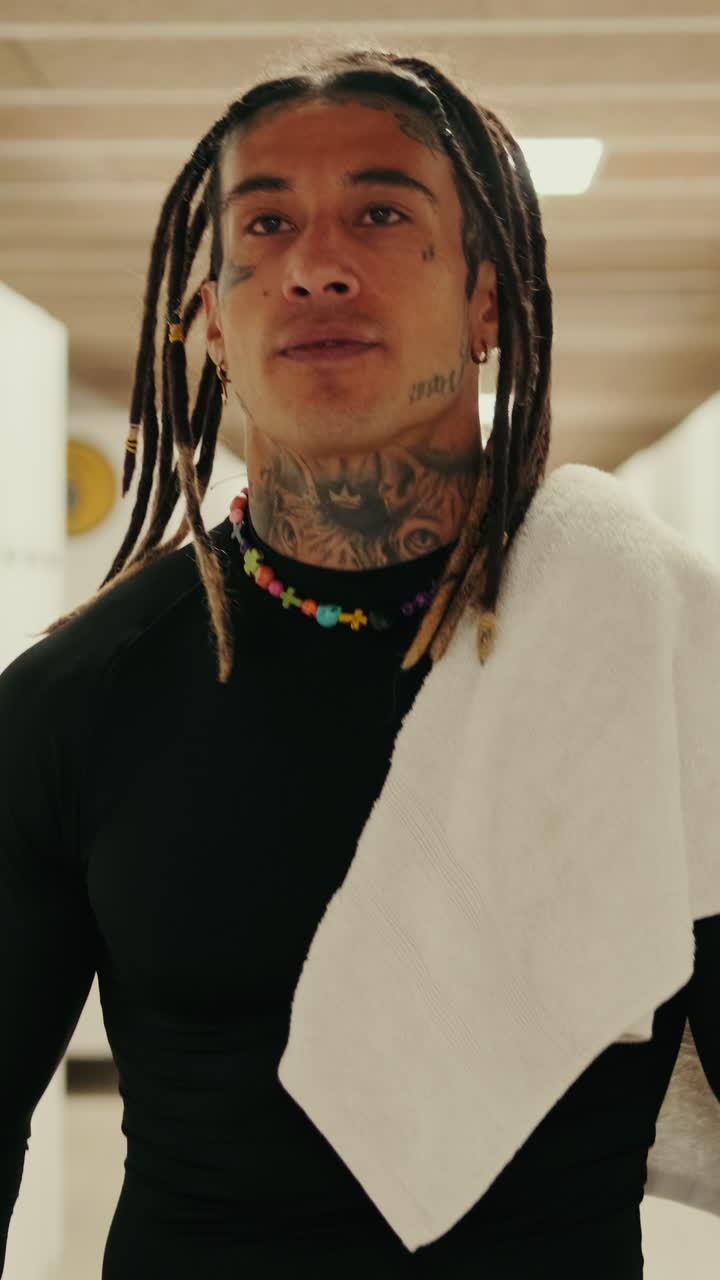 Uomo sicuro di sé con dreadlock e tatuaggi che cammina nello spogliatoio