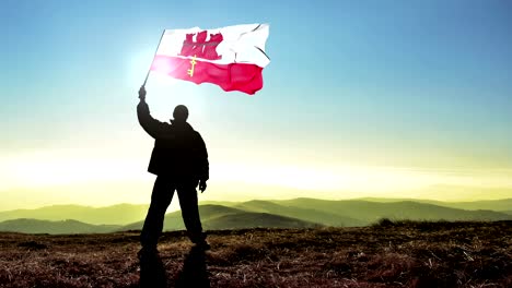 hombre de silueta exitoso ganador agitando la bandera de gibraltar en la parte superior del pico de la montaña. fondo de bucle cinemagraph