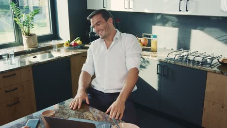 Cheerful-man-talking-at-laptop-in-kitchen.-Smiling-person-having-online-chat.