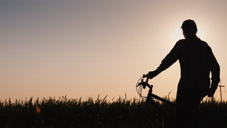 La-Silueta-De-Una-Mujer-Con-Una-Bicicleta-De-Pie-En-Un-Campo-Mirando-La-Puesta-De-Sol