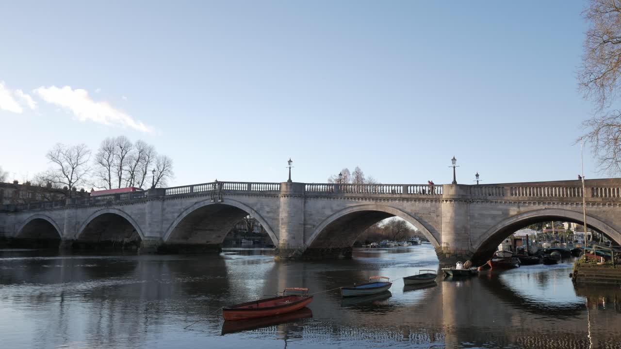 A stone bridge over a calm river with boats and trees on a clear sunny day