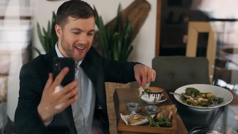 handsome young man shoots video on smartphone sitting in restaurant and eating salad with snacks