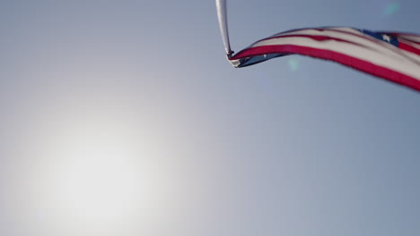 waving the american flag on a pole against the blue sky