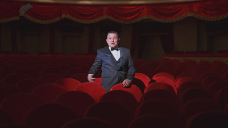 man in empty theater. rich man in suit taking off facial mask and says something among rows of red seats in the theater without audience. world crisis at pandemic.