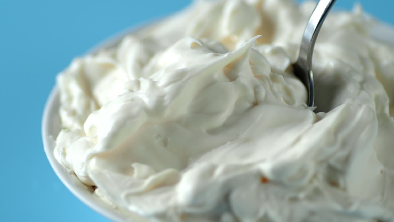 Queso mascarpone en un tazón con una cuchara girando lentamente.