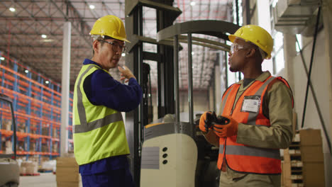 Diverse-male-workers-wearing-safety-suits-and-talking-in-warehouse